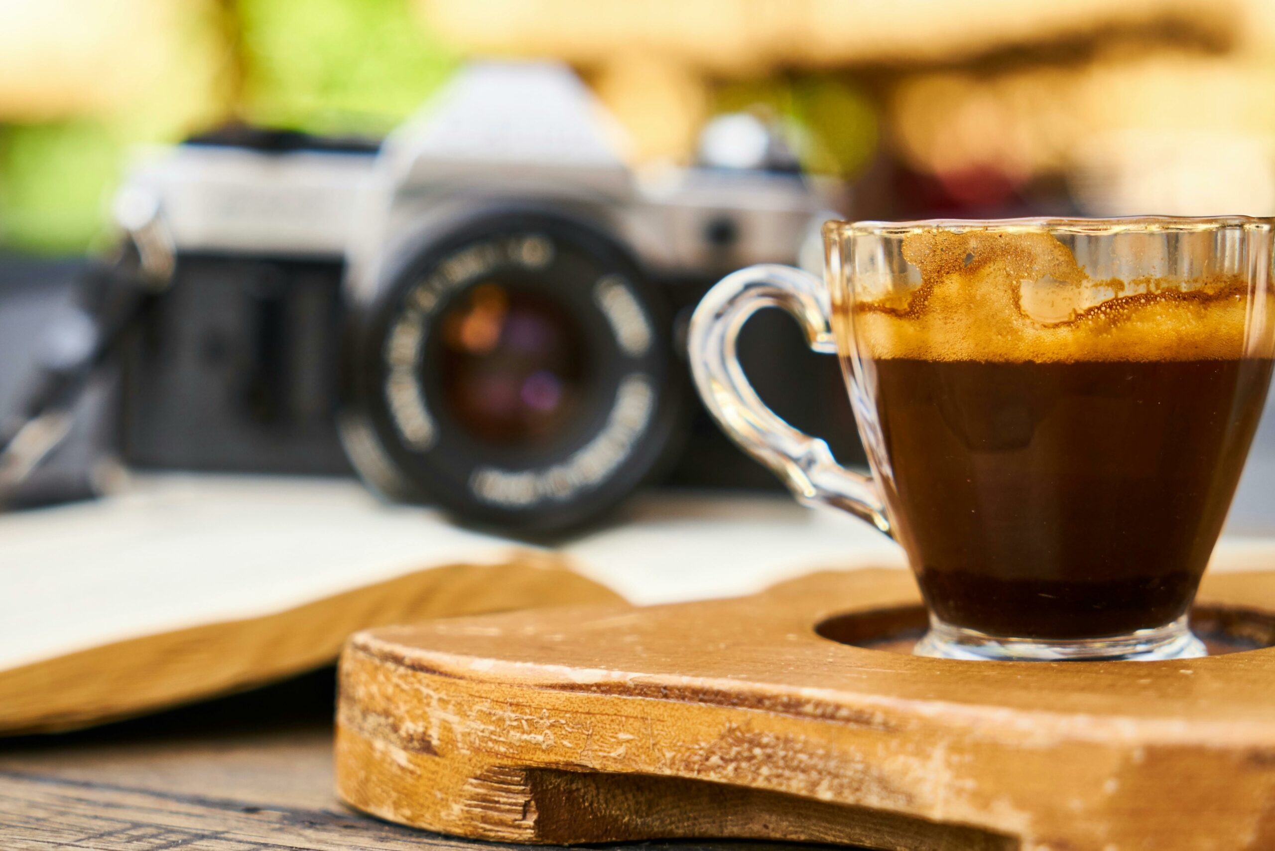 A close-up shot of a rich espresso in a glass cup next to a vintage camera on a wooden table.